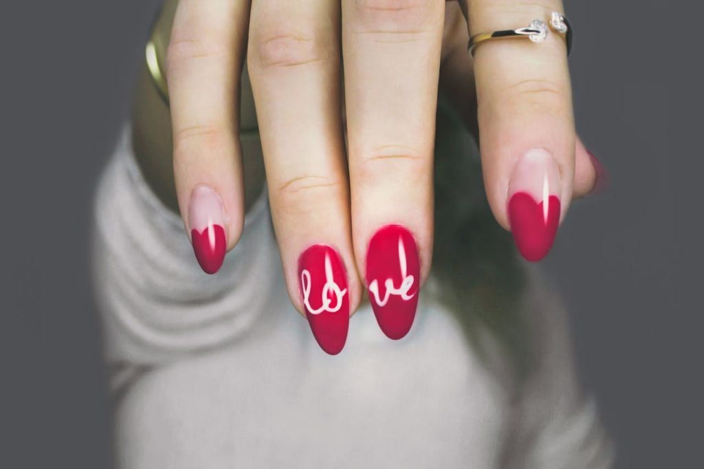Vibrant red nails with love art on a womans hand, showcasing elegant style and design.